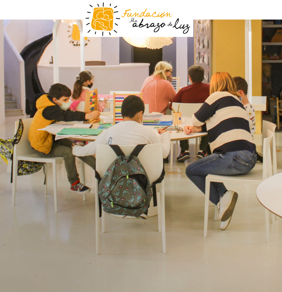 Niños en diferentes mesas con profesores haciendo deberes
